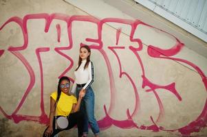 Weißes kaukasisches Mädchen und schwarzer Afroamerikaner zusammen gegen Graffitiwand. Einheit der Welt, Rassenliebe, Verständnis in Toleranz und Zusammenarbeit der Rassenvielfalt. foto