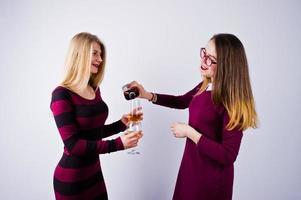 Zwei attraktive Freundinnen in lila Kleidern trinken Sekt oder Champagner im Studio. foto