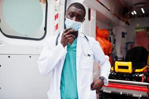 afrikanischer männlicher sanitäter mit gesichtsschutzmaske, der vor dem krankenwagen steht. foto