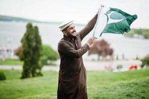 Pakistanischer Pathan-Mann trägt traditionelle Kleidung und hält die pakistanische Flagge. foto