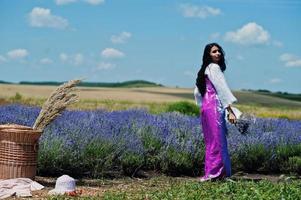 schöne indische Mädchen tragen Saree Indien traditionelles Kleid in lila Lavendelfeld mit Korb. foto