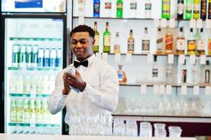 afroamerikanischer barkeeper trägt an der bar eine fliege, die eine brille putzt. foto