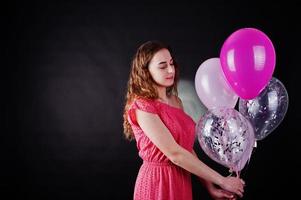 junges Mädchen im roten Kleid mit Luftballons vor schwarzem Hintergrund im Studio. foto