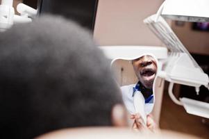 afrikanisch-amerikanischer Patient im Behandlungsstuhl. konzept für zahnarztpraxis und arztpraxis. mann, der zahn im spiegel betrachtet. foto