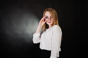 Studioporträt einer blonden Geschäftsfrau mit Brille, weißer Bluse und schwarzem Rock vor dunklem Hintergrund. erfolgreiche frau und stilvolles mädchenkonzept. foto