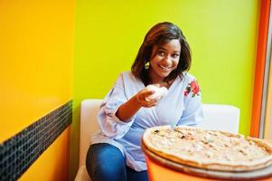 afrikanische frau gießt salz auf pizza, während sie in einem hellen restaurant sitzt. foto