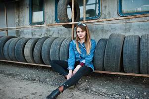 Junges Hipster-Mädchen in Jeansjacke und Kopftuch in der Reifenmontagezone. foto