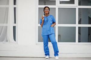 Porträt einer glücklichen afroamerikanischen jungen Ärztin, Kinderärztin in blauem Uniformmantel und Stethoskop gegen Fenster im Krankenhaus. gesundheitswesen, medizin, medizinspezialist - konzept. foto