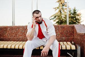 junger brutaler bärtiger muskulöser mann trägt einen weißen sportanzug mit rotem hemd. foto