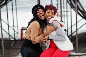 Zwei afroamerikanische Frauen posierten am Wintertag vor schneebedecktem Hintergrund mit Tassen Kaffee. foto