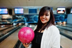 stilvolle asiatische frau, die an der bowlingbahn mit ball zur hand steht. foto