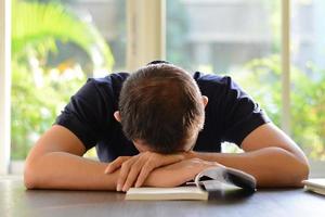 junger Mann, der mit geöffnetem Buch auf dem Tisch schläft foto