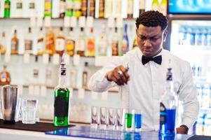 Afroamerikanischer Barkeeper an der Bar, der Cocktails auf Aufnahmen macht. Zubereitung von alkoholischen Getränken. foto