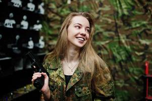 Militärmädchen in Tarnuniform mit Waffe zur Hand vor Armeehintergrund auf Schießstand. foto