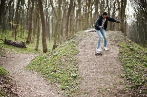 arabischer Streetstyle-Mann mit Brille und Longboard auf Holz. foto