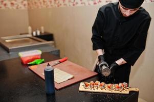 professionelle kochkleidung in schwarz, die sushi und brötchen in einer restaurantküche mit japanischer traditioneller küche herstellt. foto