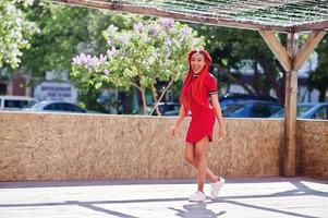 süßes und schlankes afroamerikanisches Mädchen in rotem Kleid mit Dreadlocks in Bewegung, das Spaß auf der Straße hat. stylisches schwarzes Modell. foto