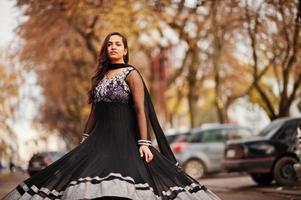 hübsches indisches mädchen im schwarzen saree-kleid posierte im freien auf der herbststraße. foto