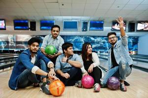 gruppe von fünf südasiatischen völkern, die sich im bowlingclub ausruhen und spaß haben und mit bällen auf den händen auf der bowlingbahn sitzen. foto