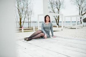 Porträt eines brünetten Mädchens in grauem Kleid, das an einer weißen Holzkonstruktion sitzt. foto