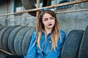 Junges Hipster-Mädchen in Jeansjacke und Kopftuch in der Reifenmontagezone. foto