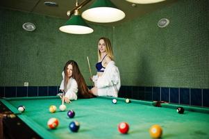 Zwei sexy Girls in weißem Bademantel und Badeanzug spielen Billard. foto