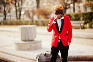 Mode-Afroamerikaner-Mann-Model im roten Anzug, mit Highlights Haar und Handtasche auf der Straße gestellt. foto