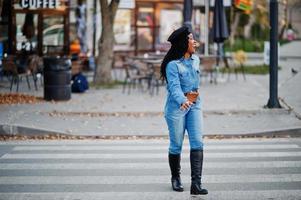 stilvolle modische afroamerikanische frauen in jeans und schwarzer mütze, die auf dem fußgängerverkehr laufen. foto