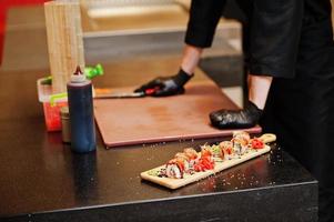 Nahaufnahme der Hände professioneller Köche in schwarzen Handschuhen, die Sushi und Brötchen in einer Restaurantküche mit japanischer traditioneller Küche zubereiten. foto