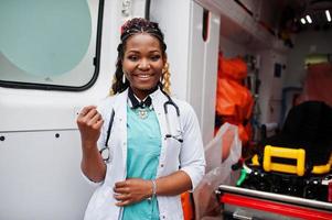 Afroamerikanische Sanitäterin, die vor einem Krankenwagen steht. foto