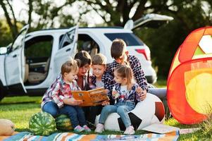 familie verbringt zeit zusammen. mutterlesebuch im freien mit kindern gegen ihr suv-auto. foto