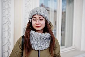 Porträt eines brünetten Mädchens in grauem Schal und Hut, Brille bei kaltem Wetter. foto