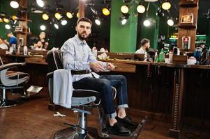 hübscher bärtiger mannfriseur, der auf stuhl im friseursalon sitzt. foto