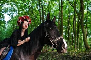 mystisches mädchen in kranzabnutzung in schwarz am pferd im holz. foto