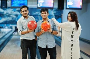 drei südasiatische freunde im jeanshemd im bowlingclub, die bälle an den händen halten. foto