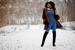 lockiges haar afroamerikanerin trägt schaffellmantel und handschuhe, die am wintertag gestellt werden. foto