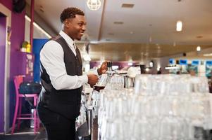 Afroamerikanischer Barkeeper an der Bar, der im Pub frisches Bier vom Fass in das Glas gießt. foto