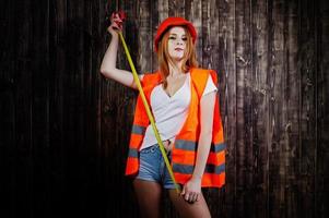 ingenieurin in orange schützt helm und baujacke vor hölzernem hintergrund mit maßband. foto