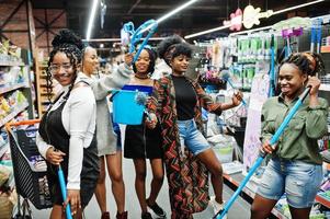 gruppe von fünf afrikanischen frauen mit staubmopp, toilettenbürste und eimer, die spaß in der abteilung für haushaltsreinigungsartikel im supermarkt haben. foto