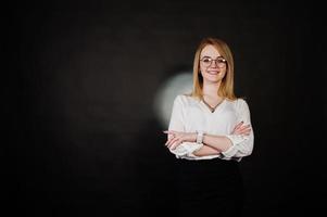 Studioporträt einer blonden Geschäftsfrau mit Brille, weißer Bluse und schwarzem Rock vor dunklem Hintergrund. erfolgreiche frau und stilvolles mädchenkonzept. foto