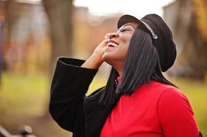 Nahaufnahme Porträt eines afroamerikanischen Modemädchens in Mantel und Zeitungsjungenkappe, das auf der Straße posiert. foto