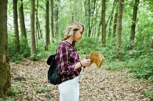 Porträt einer jungen schönen blonden Frau im Tartanhemd mit einer Karte im Wald. foto