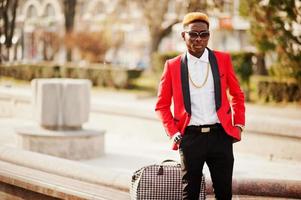 Mode-Afroamerikaner-Mann-Model im roten Anzug, mit Highlights Haar und Handtasche auf der Straße gestellt. foto