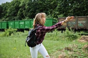 Porträt einer jungen Blondine im Schottenkaro-Hemd neben dem Zug mit einer Karte. foto