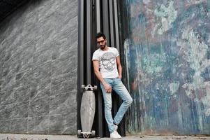 arabischer mann im streetstyle mit brille und longboard posiert. foto