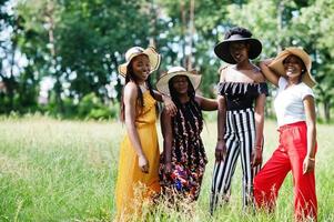 eine gruppe von vier wunderschönen afroamerikanischen frauen trägt einen sommerhut, der zeit auf grünem gras im park verbringt. foto