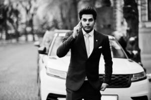 elegantes indisches macho-mann-modell auf anzug und rosa krawatte posierte vor weißem geschäftsauto und sprach am telefon. foto