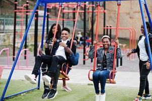 junge tausendjährige afrikanische freunde auf spielplatz, rutsche und schaukel. glückliche schwarze leute, die zusammen spaß haben. generation z freundschaftskonzept. foto