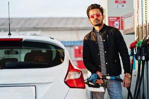 südasiatischer mann oder indischer mann, der sein weißes auto an der tankstelle betankt. foto