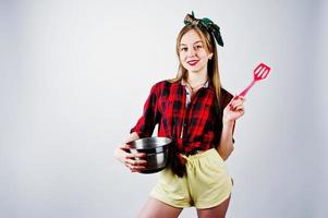 junge lustige Hausfrau in kariertem Hemd und gelben Shorts Pin-up-Stil mit Topf und Küchenlöffel isoliert auf weißem Hintergrund. foto